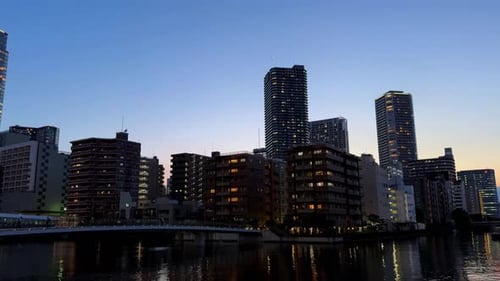 City skyline at dusk with lit buildings reflected on a calm river