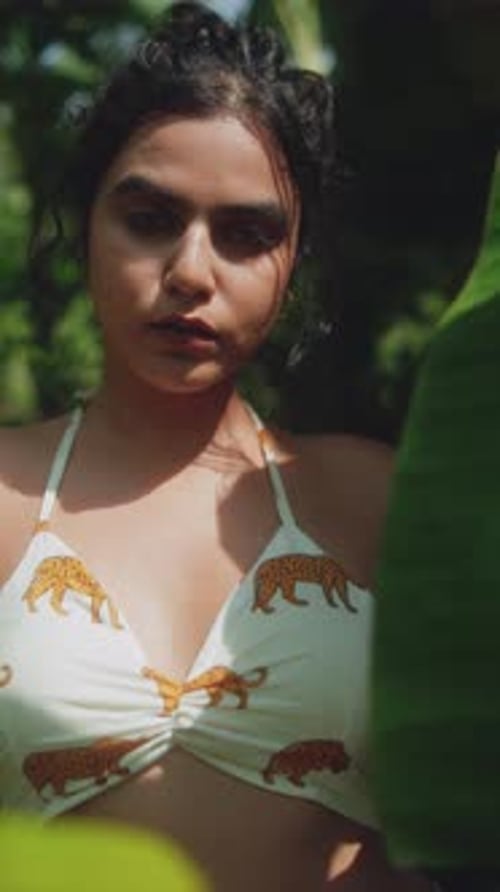 Portrait of young woman in tropical outfit among lush green leaves on sunny day