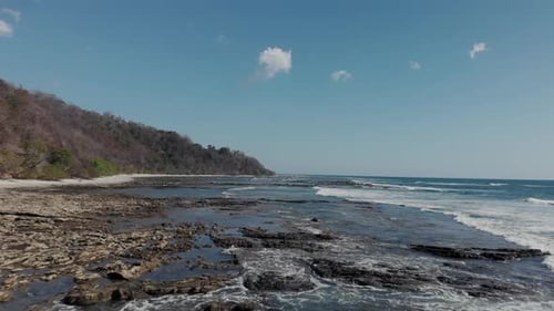 Waves On The Rocky Coast Of Costa Rica Beach With Blue Sky On The Background.- aerial drone shot