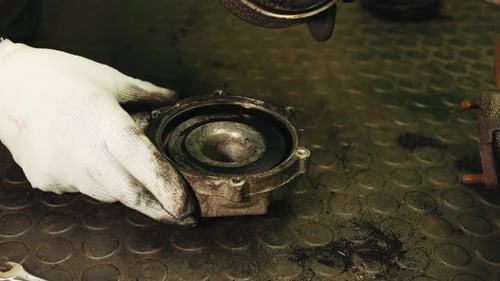 Car mechanic in white gloves disassembles inside the car engine part turbine filled with rust