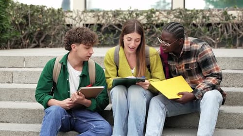 Étudiants universitaires assis sur l'escalier travaillant et apprenant ensemble en vue des examens