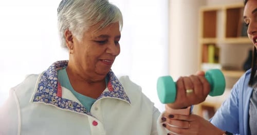 Senior Woman Lifting Weights with Young Adult Assistant
