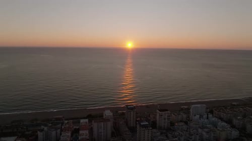 Drone view of the sunset on the horizon over the sea or ocean near a coastal city