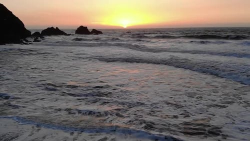 A drone flying backwards and capturing footage of the sunset in the ocean, and revealing a hiker wit