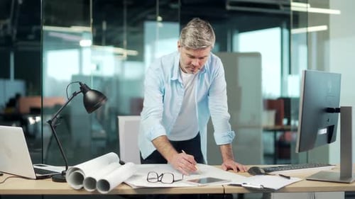 mature creative designer, architect working in the office at work a computer desk with drawings.