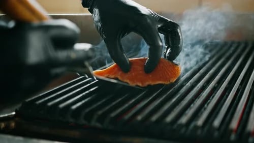 Professional kitchen in restaurant close-up chef flips juicy piece of fresh grilled salmon texture
