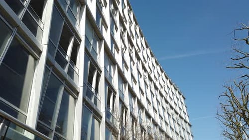 Low angle view panning across high business office buildings to blue sky. Glass window fronts reflec