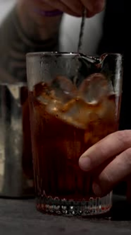 Bartender stirs cocktail with ice in glass
