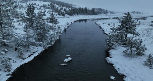 An Aerial View of a Frozen River Flowing Through Snowcovered Forests on a Cloudy Sunset Sky