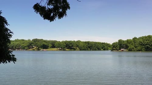 Reveal from behind branches of a beautiful scenic lake with trees surrounding the shoreline.