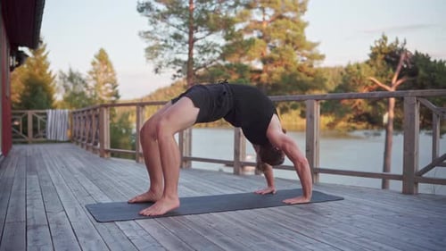 Postura de yoga con ruedas: hombre haciendo flexiones hacia atrás sobre la colchoneta de yoga. Foto panorámica