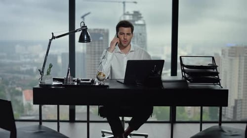 Smiling businessman talking smartphone in modern office with city view