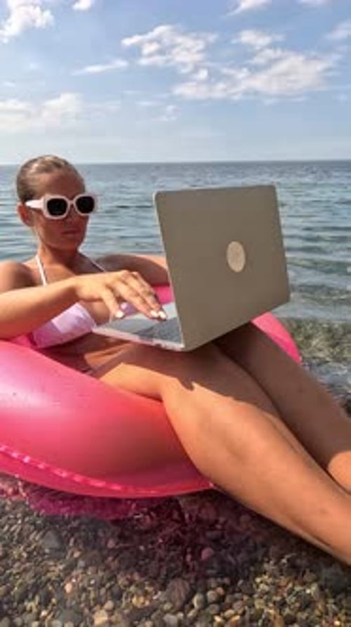 Woman Freelancer Works on Laptop Swimming in Sea on Pink Inflatable Ring Happy Tourist in Sunglasses
