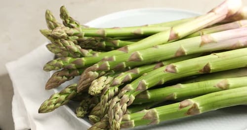 Fresh raw asparagus spinning on light grey table, closeup