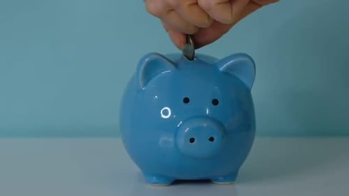 Piggy Bank Business Concept A Hand is Putting a Coin in a Piggy Bank on a Blue Background Saving