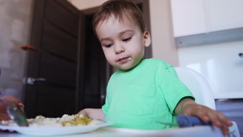 Adorable Child Eats Meal in Kitchen with Parent