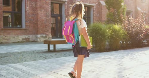 Little girl with backpack and textbook going hurrying to school. Attaractive schoolgirl with backpac