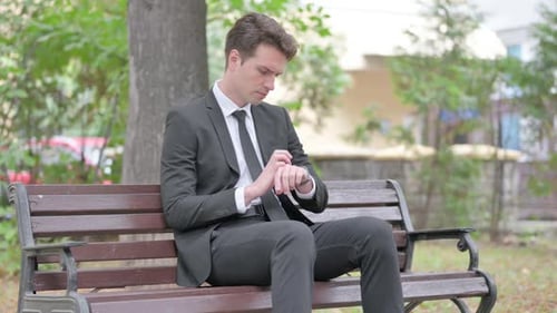 Man Checking Watch on Park Bench in Suit