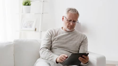 Senior Man Relaxing on Sofa Using Tablet