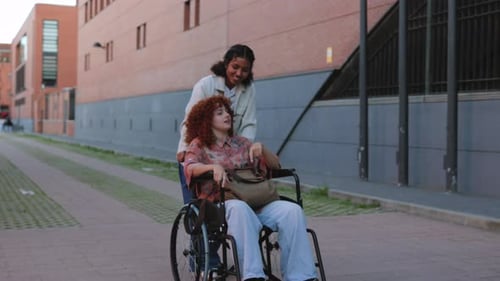 Happy multi ethnic friends are walking down the street, a young woman is pushing her red haired frie