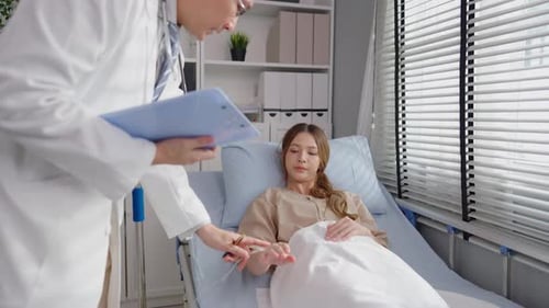 Asian male doctor examine patient woman lying on bed in recovery room.
