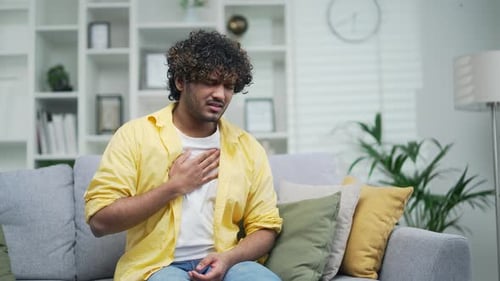 A young male is suffering from heartburn the handsome man is holding his chest and feels pain and pr