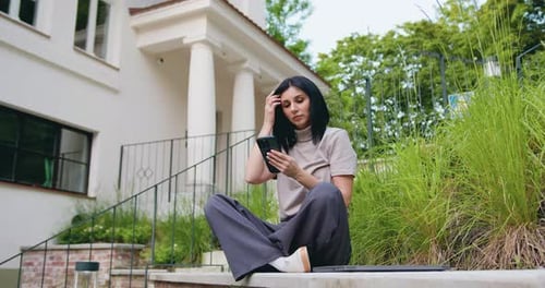 Young lady in casual clothes focused on her phone with a subtle smile, residential building