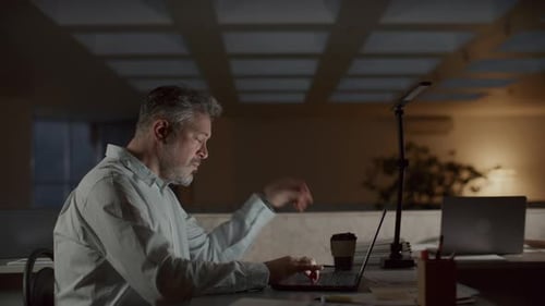 Empresário cansado fechando laptop, saindo do local de trabalho do escritório à noite