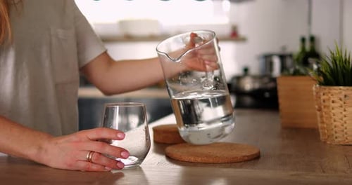 Woman Pours Water into Glass Cup in Kitchen