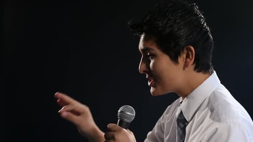 Young Man Speaking Into Microphone on Dark Background