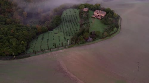 Aerial view of misty countryside with villa and cypress trees, Italy.