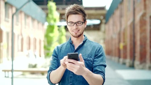 Handsome young man uses a smartphone Stands on the street. Happy cheerful guy student in casual
