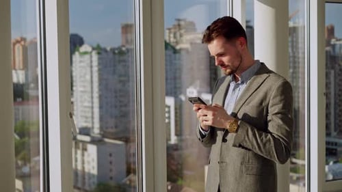 A Successful Young Businessman in a Nice Suit in the Office Near the Window Picks Up the Phone and