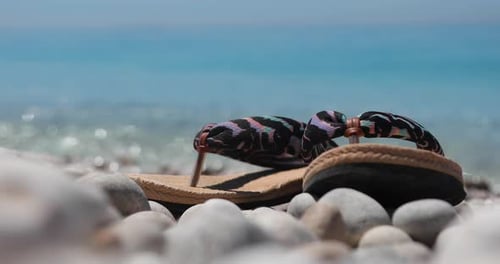 Urlaubskonzeptfoto, Flip-Flops am ruhigen Kiesstrand mit smaragdgrünem Meereshintergrund