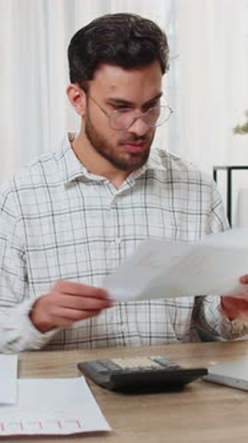 Focused Indian Office Worker Working with Schedules and Financial Graphics While Using Calculator