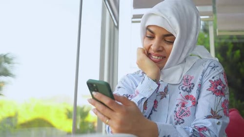 Schöne glückliche muslimische arabische Hijab-Frau nutzt Smartphone in Innenräumen Konzept der sozialen Medien im Internet