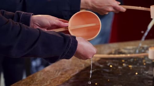 Close up of people performing the purification ritual at a water fountain at the Senso-ji temple in
