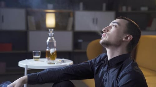 Un jeune homme malheureux fume une cigarette.