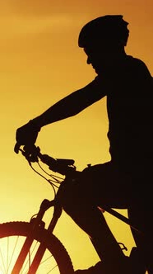 Silhouette of professional bicyclist taking a bottle and drinking water at golden sunset.