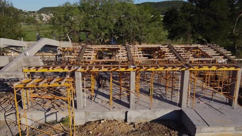 Proceso constructivo de vigas de hormigón armado y encofrado de madera con andamio amarillo sobre una s