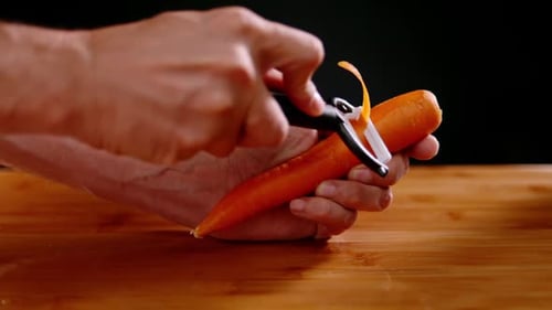 Person hand peeling fresh orange carrot using peeling tool, slow motion view