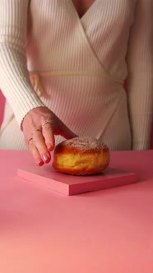 Close-up of a woman's hand with rings and manicured nails grabbing a sugar-coated Berliner donut