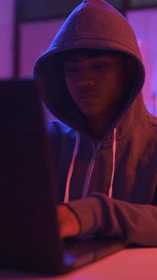 Ein mysteriöser Hacker mit Kapuze, der an einem Computer in einem dunklen Raum arbeitet.