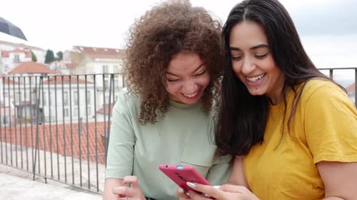 Two Smiling Women Look at Phone in Urban Setting
