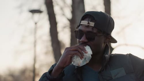 Man with dreadlocks eating sandwich outdoors in park