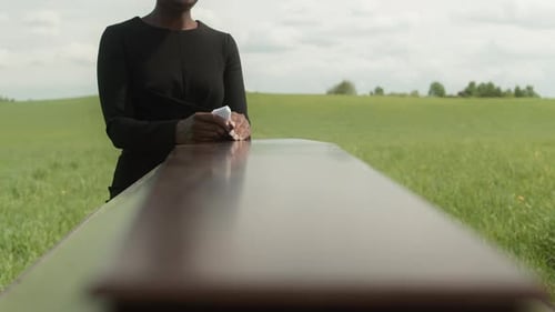 Mournful Woman Stands by Casket Outdoors in Grassy Field