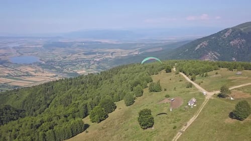 Aerial view from drone of athlete paragliding. Person under large green parachute floating close to