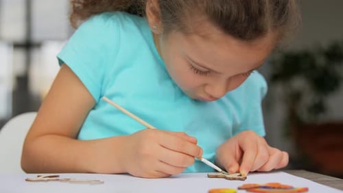 Girl Painting Wooden Toy with Brush on Paper