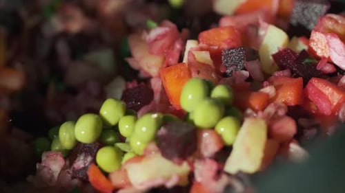 Green peas fall into the bowl with red salad, close up view