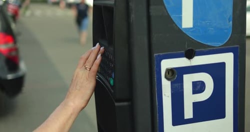Hand Entering Data on Parking Meter in City